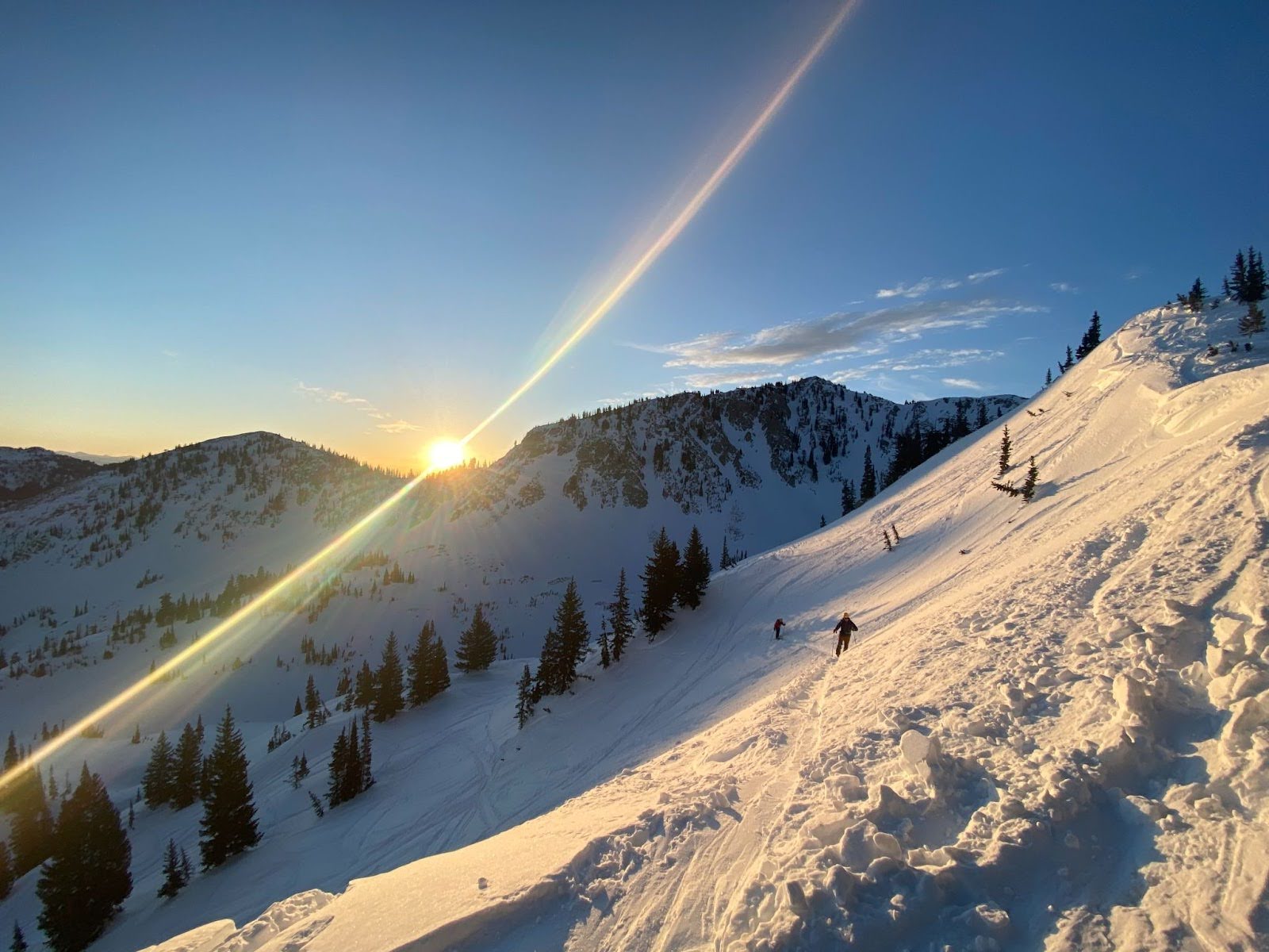 People skiing on a mountain as the sun is peeking over it